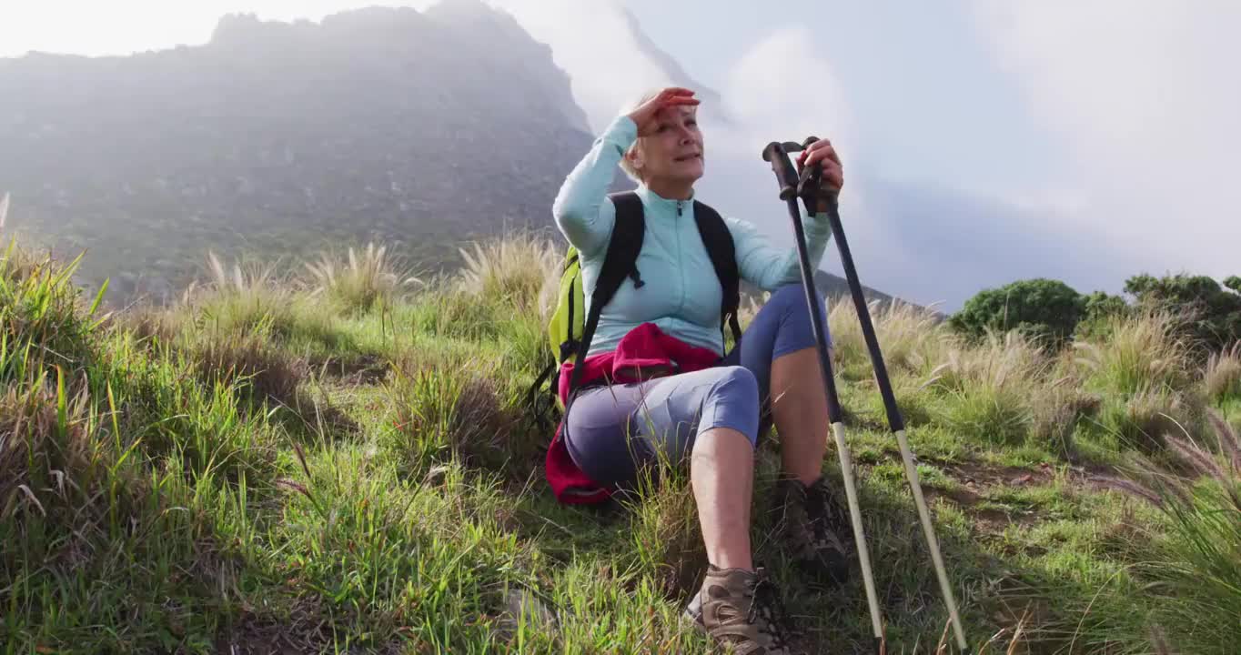 疲惫的高级徒步女坐在草地上，而徒步在山上。徒步旅行视频购买