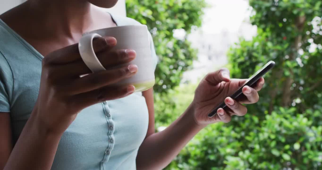 一个非裔美国女性，在家里用智能手机端着咖啡杯视频素材