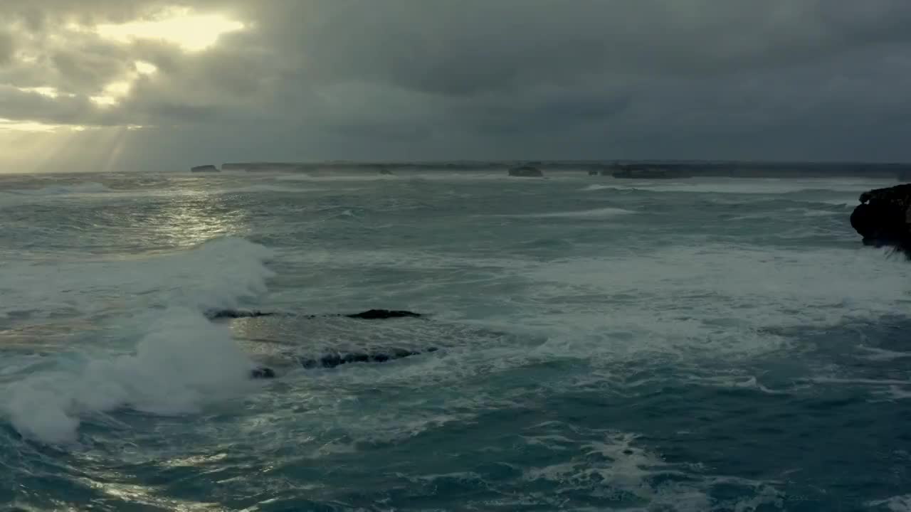 海面上的大浪打在岩石上，远处阳光从云层中漏了下来视频素材