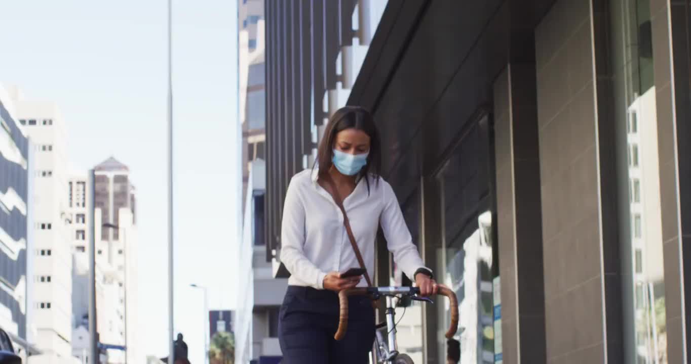 非洲裔美国妇女戴着口罩，使用智能手机自行车视频素材