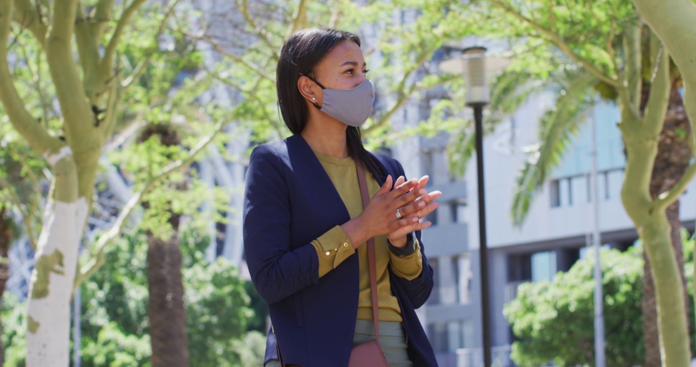 非洲裔美国妇女戴着口罩在街上给双手消毒视频素材