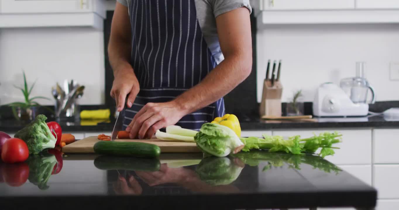 中部的白人男子穿着围裙在厨房里切菜视频素材