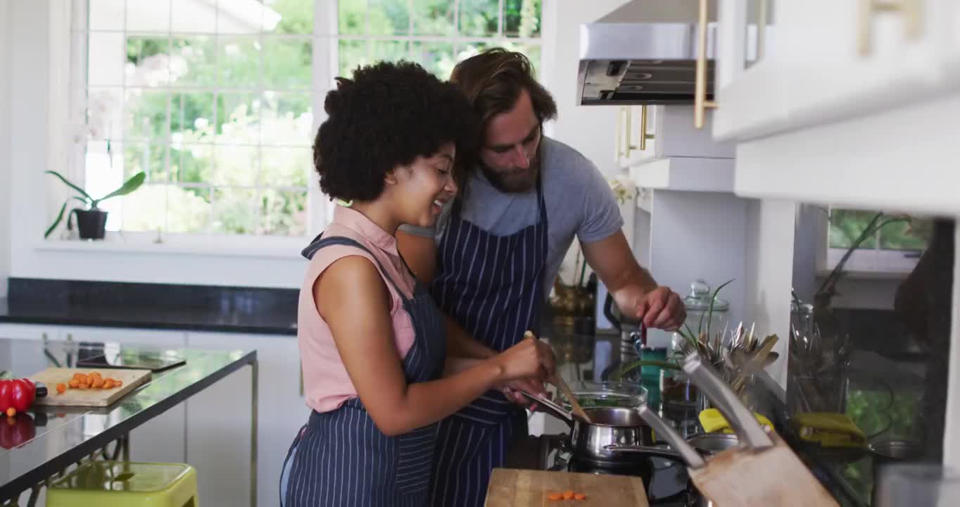 在家里的厨房里，穿着围裙的混血夫妇一起做饭视频素材