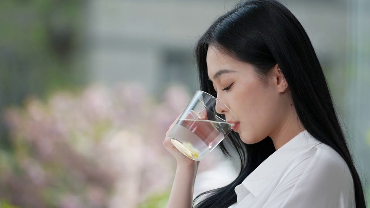 清晨，年轻女子，站在窗前端着水杯喝水，美丽优雅的青年女性。面部特写。视频下载