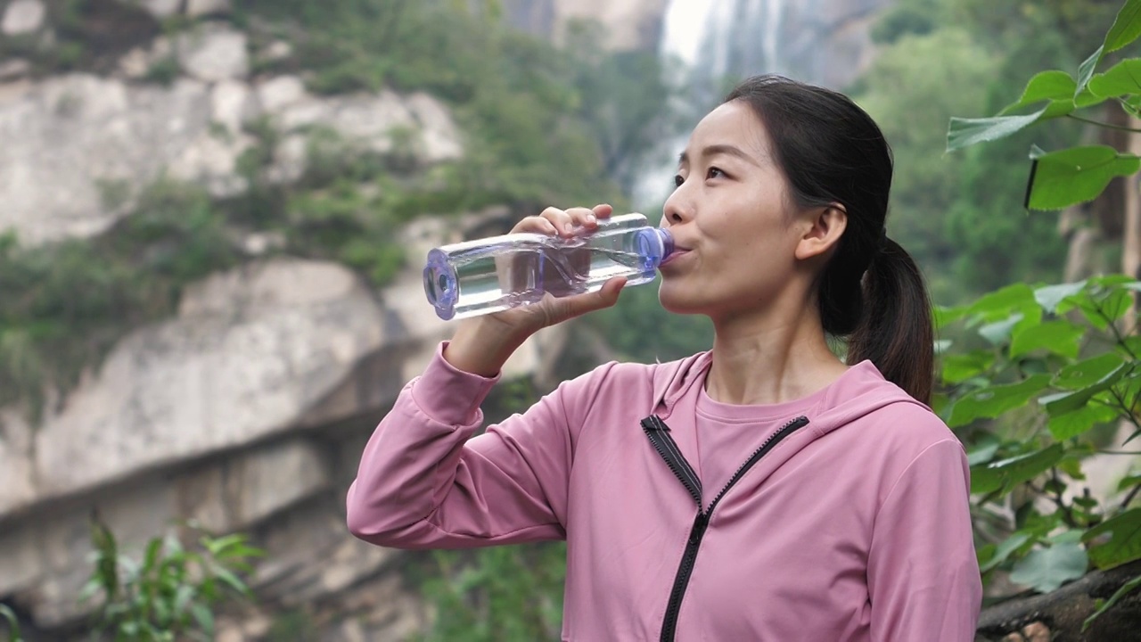 亚洲中国人女性在瀑布下喝水饮用水视频素材