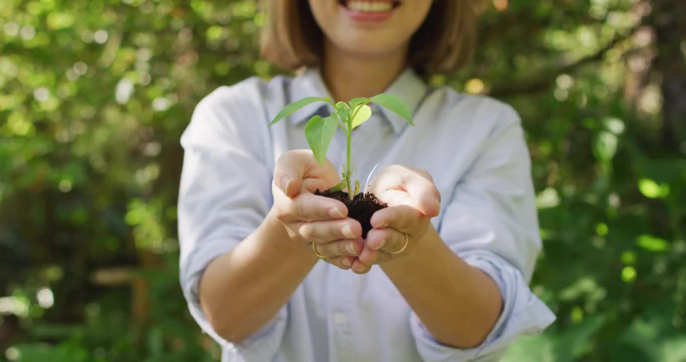 亚洲妇女在阳光明媚的日子里抱着植物在花园里微笑视频素材