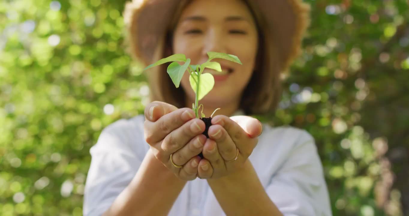 亚洲妇女在阳光明媚的日子里抱着植物在花园里微笑视频素材