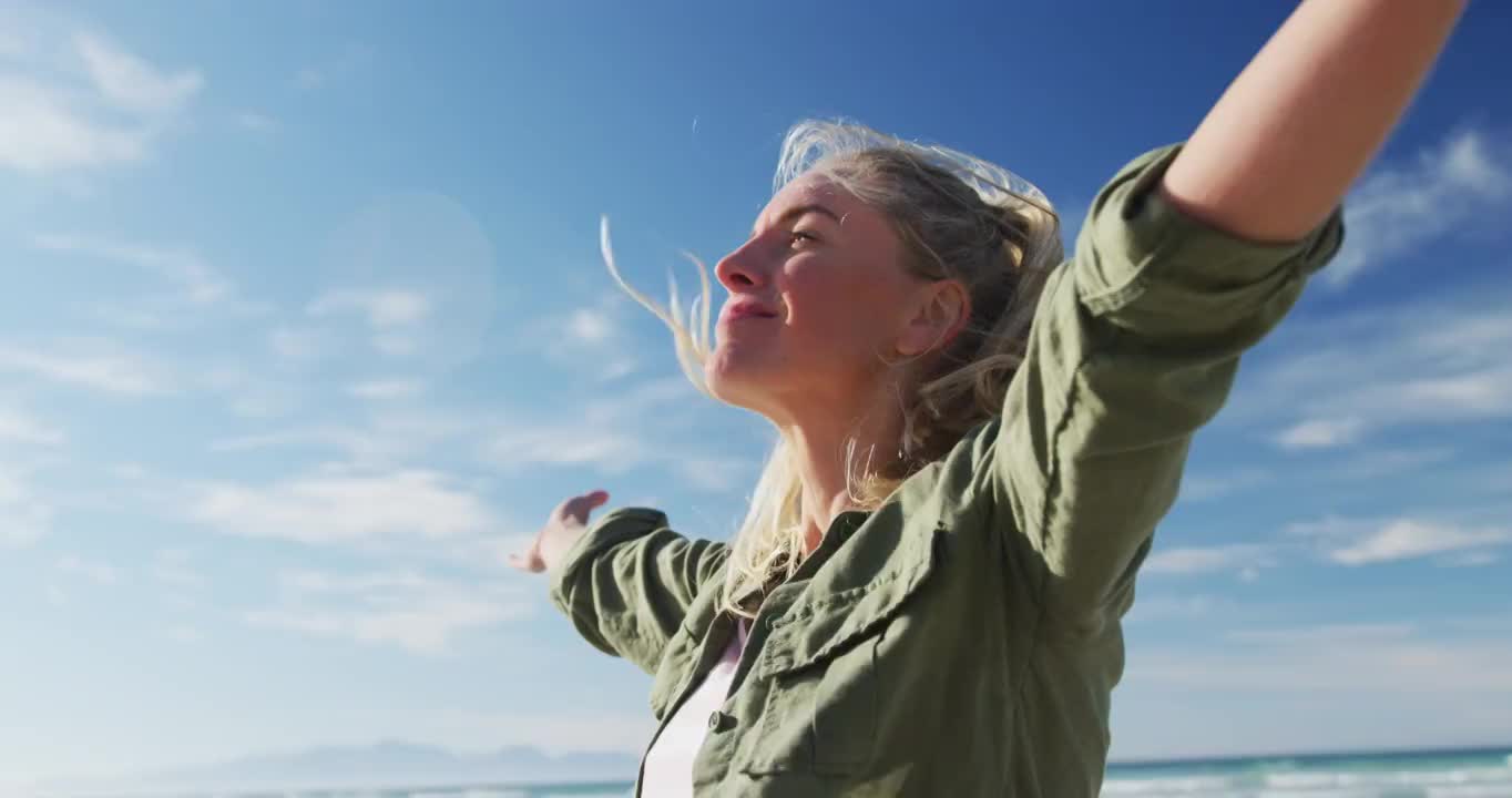 在阳光明媚的日子里，在海滩上张开双臂微笑的白人妇女视频素材