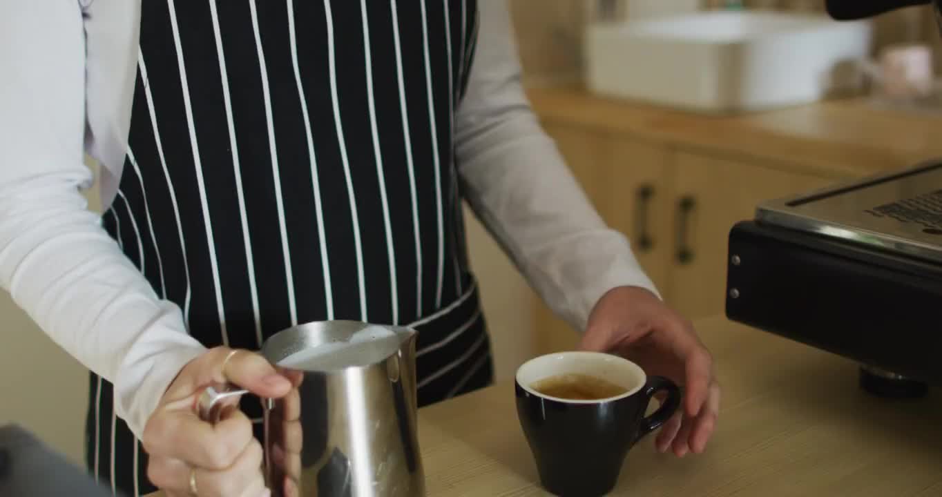 腰上系着围裙的白人女服务员，把牛奶倒进咖啡杯里视频素材