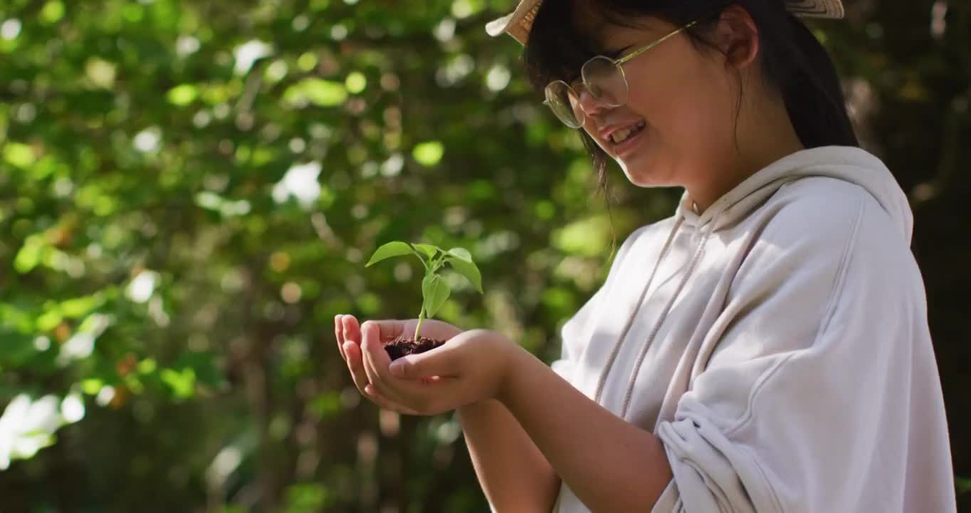 亚洲女孩在阳光明媚的日子抱着植物在花园里微笑视频素材