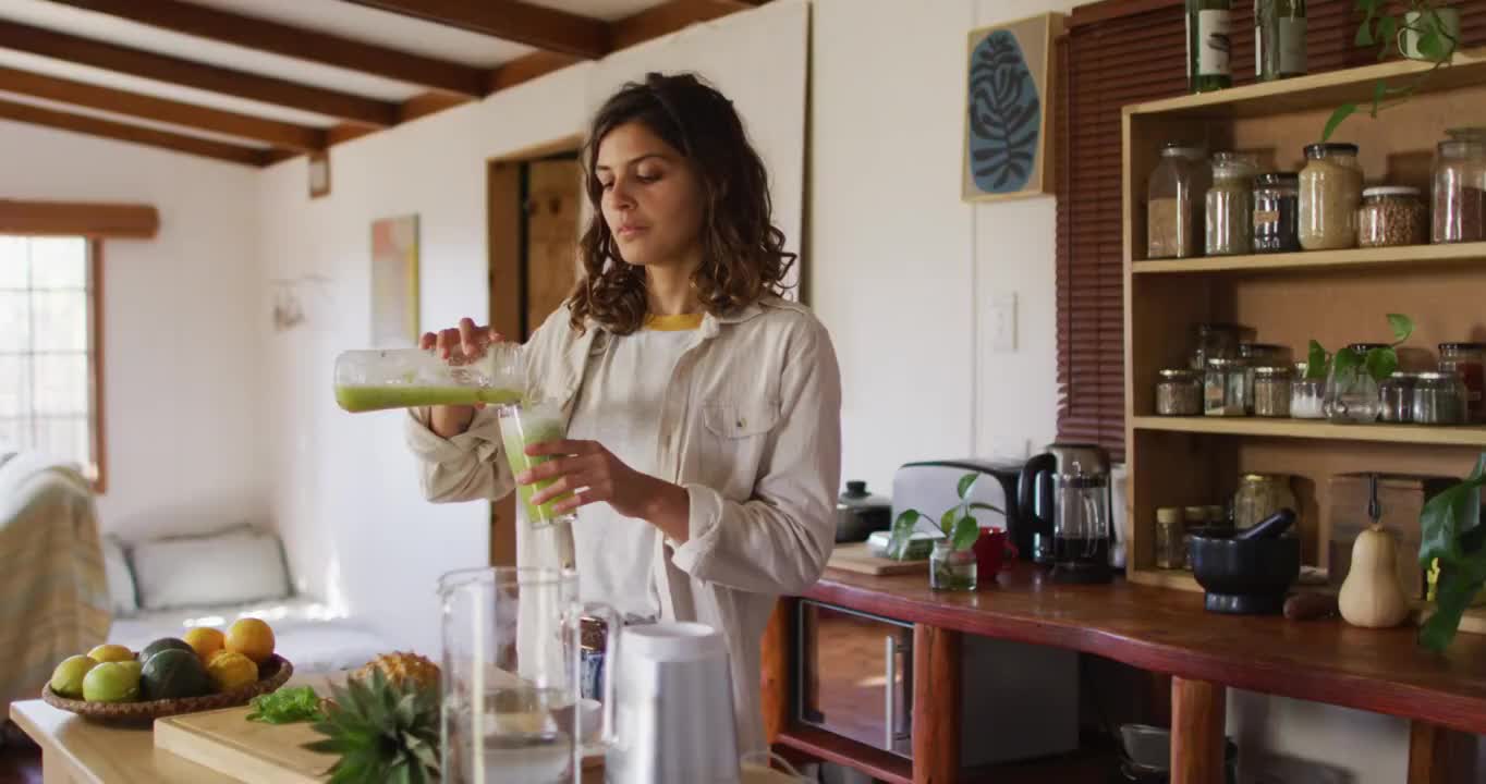 快乐的混血妇女站在村舍厨房里微笑着倒着健康饮料视频素材