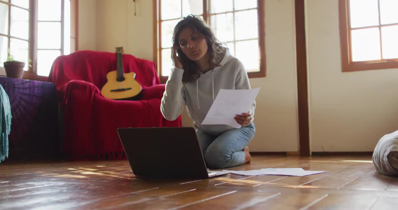 混血妇女在家工作，跪在地板上使用笔记本电脑，在小屋拿着文件视频素材