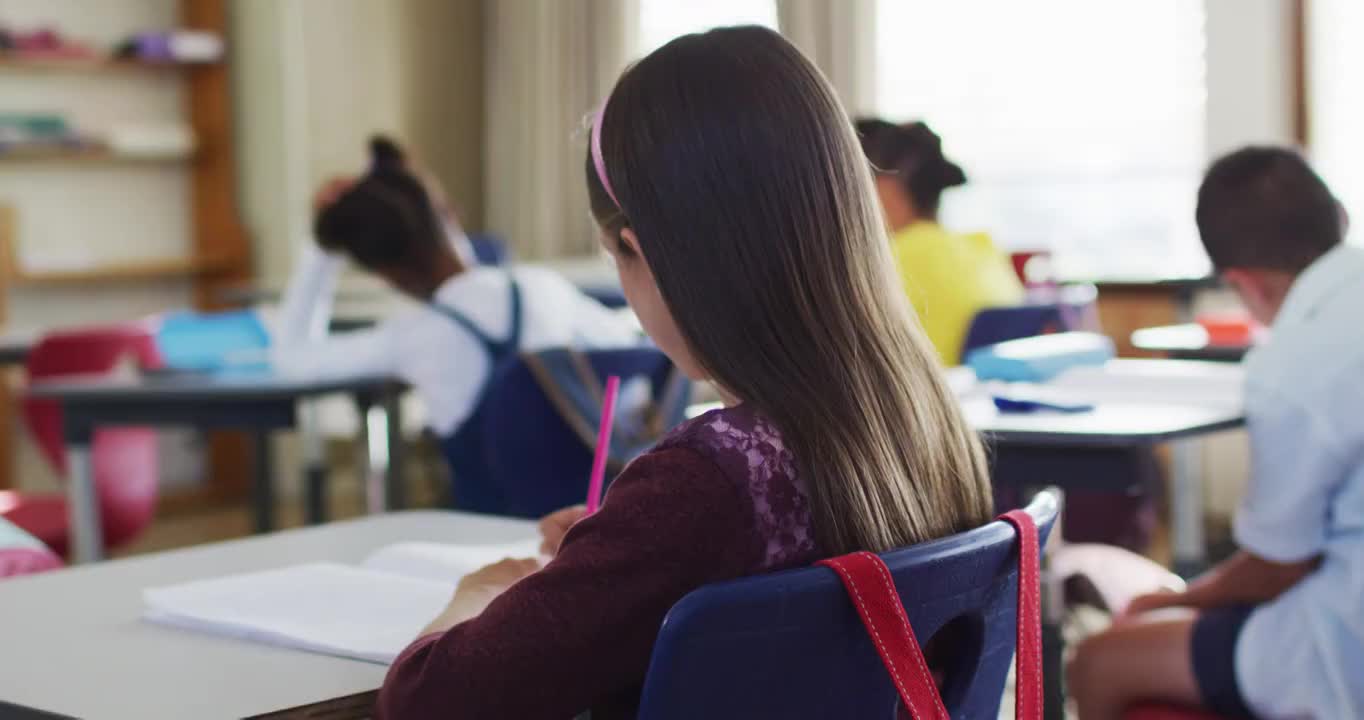 快乐的白人女学生的肖像坐在教室里，做笔记，看着相机视频素材