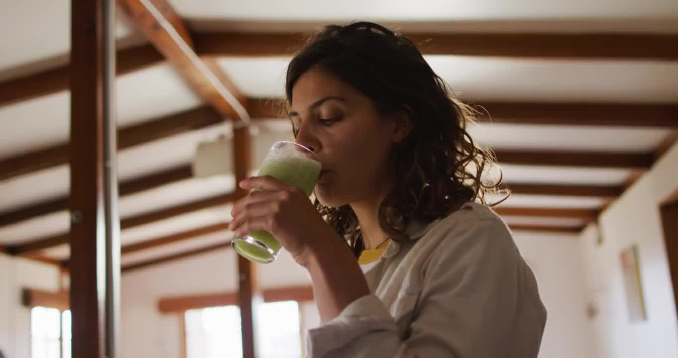 快乐的混血妇女喝着健康的饮料站在小屋的客厅里微笑着视频素材