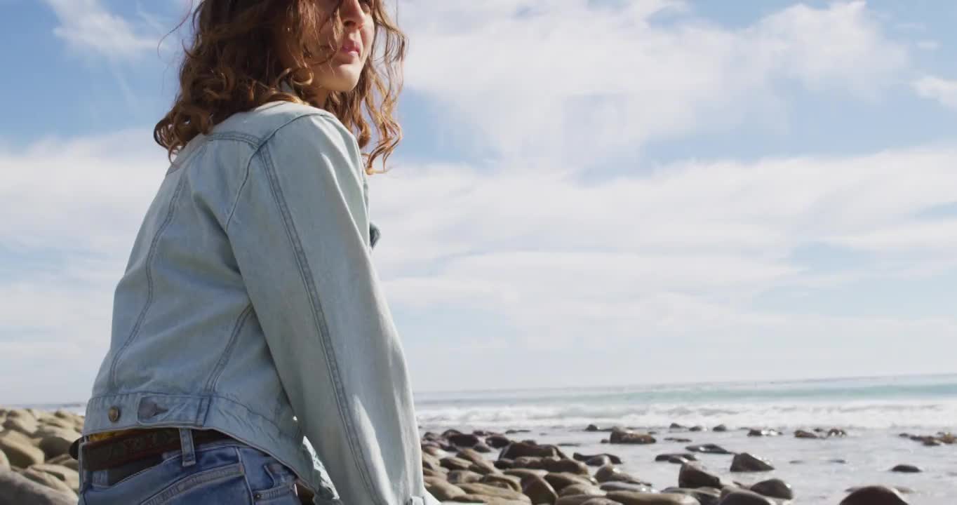 沉思的混血妇女坐在海边的海滩上，享受着风景，微笑着视频素材