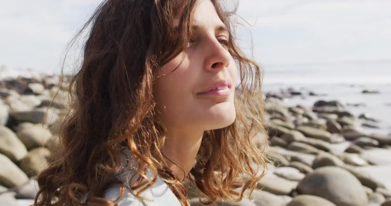 沉思的混血妇女坐在海边的海滩上，享受着风景，微笑着视频素材