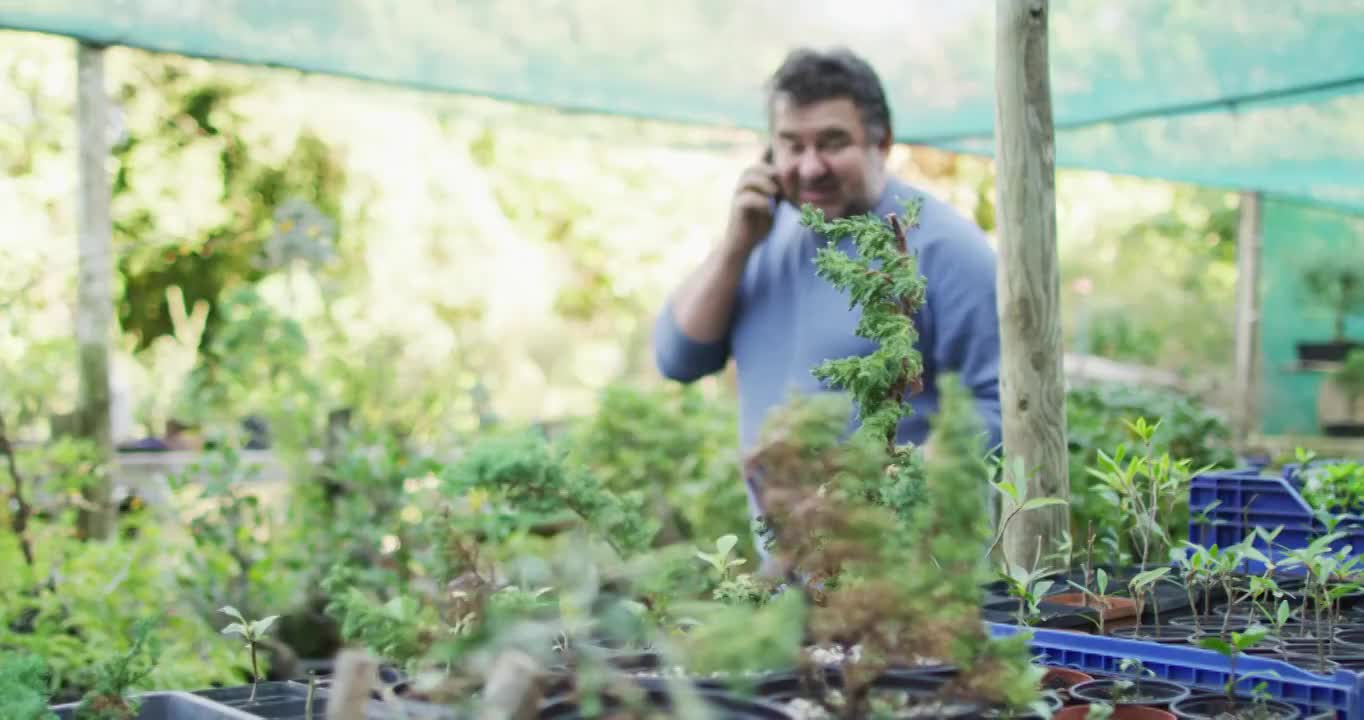 白人男性园丁检查植物和使用智能手机在花园中心视频素材