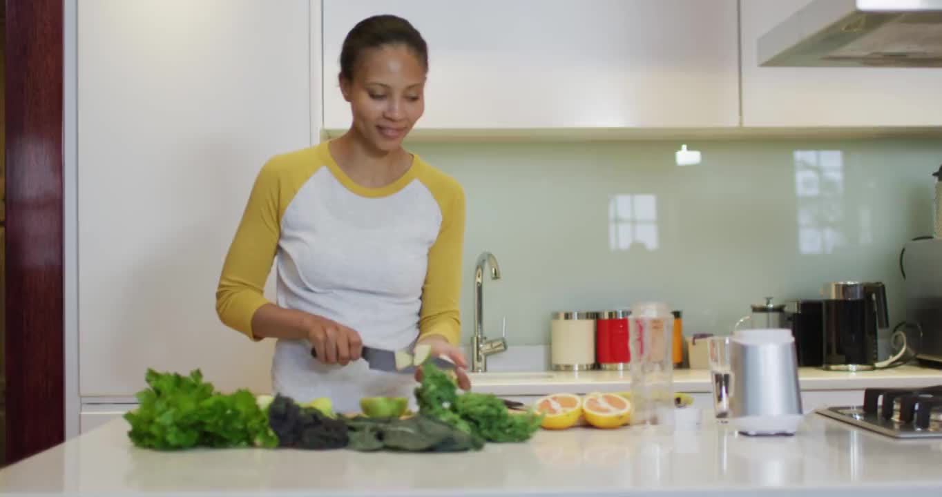 混合种族妇女准备健康的饮料，切水果和蔬菜在厨房视频素材