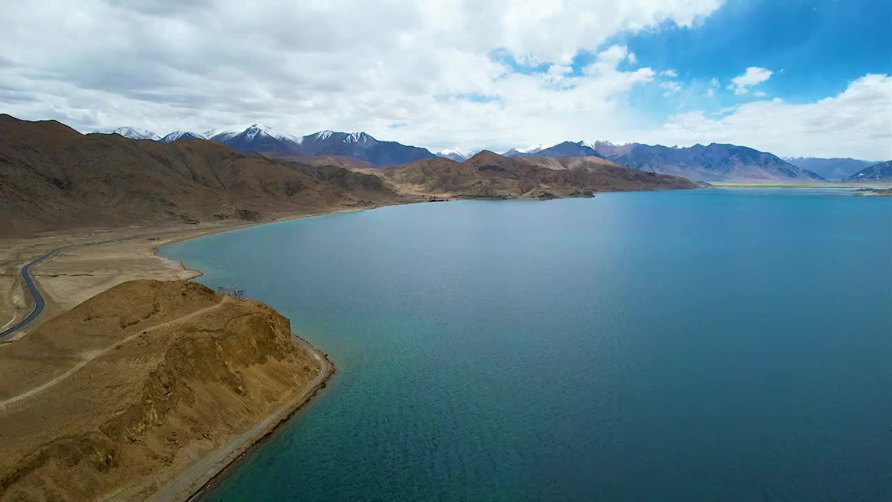 西藏阿里班公湖，六月晴朗的天气，航拍蓝天白云下，湖水湛蓝，雪山环抱，新藏公路从湖边经过。视频素材