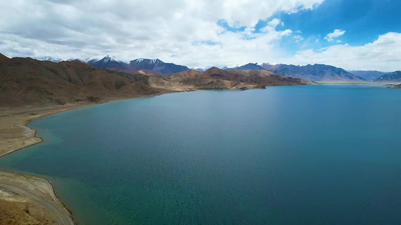 西藏阿里班公湖，六月晴朗的天气，航拍蓝天白云下，湖水湛蓝，雪山环抱，新藏公路从湖边经过。视频素材