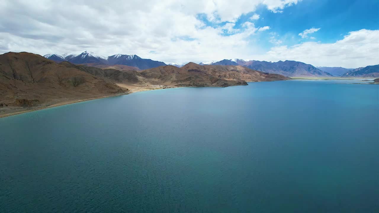 西藏阿里班公湖，六月晴朗的天气，航拍蓝天白云下，湖水湛蓝，雪山环抱，新藏公路从湖边经过。视频素材