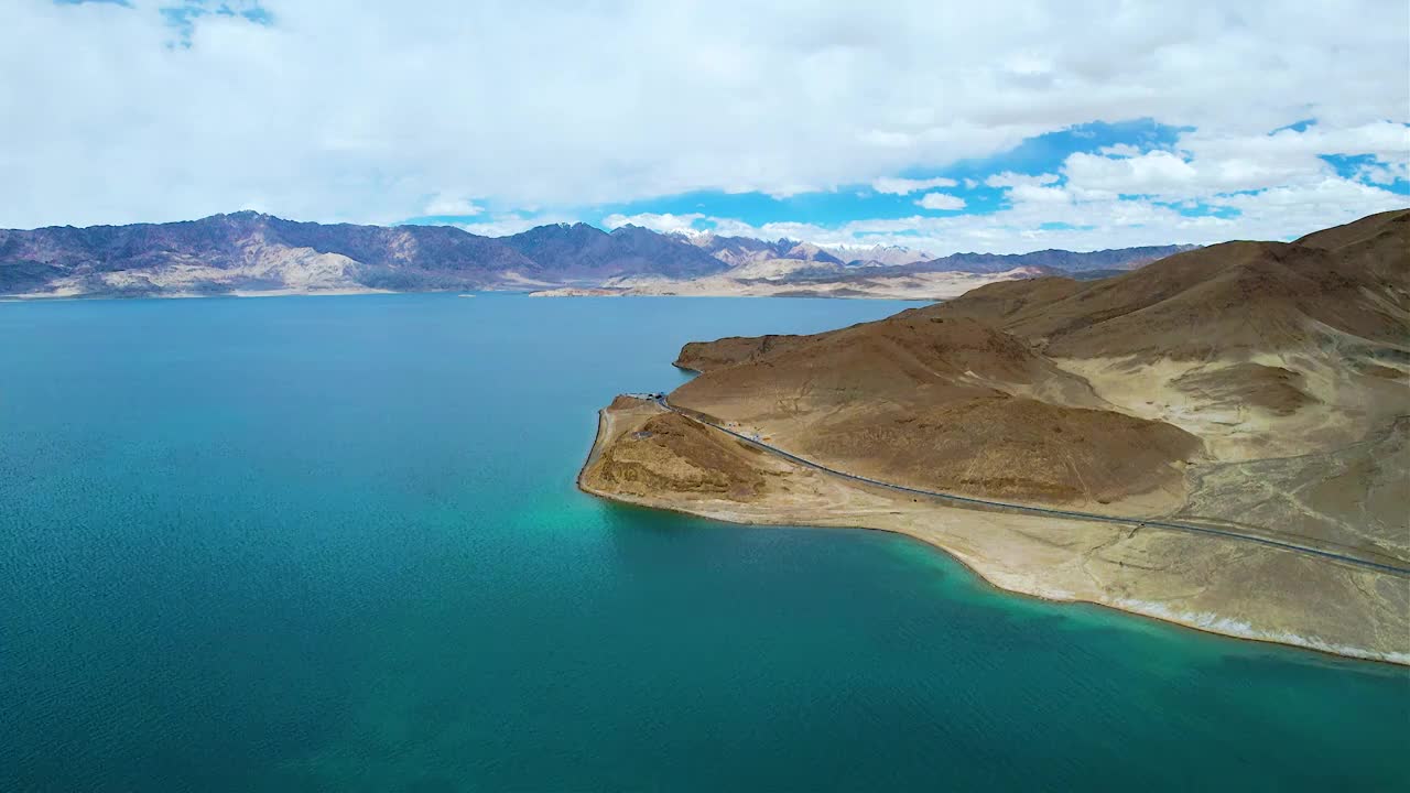 西藏阿里班公湖，六月晴朗的天气，航拍蓝天白云下，湖水湛蓝，雪山环抱，新藏公路从湖边经过。视频素材