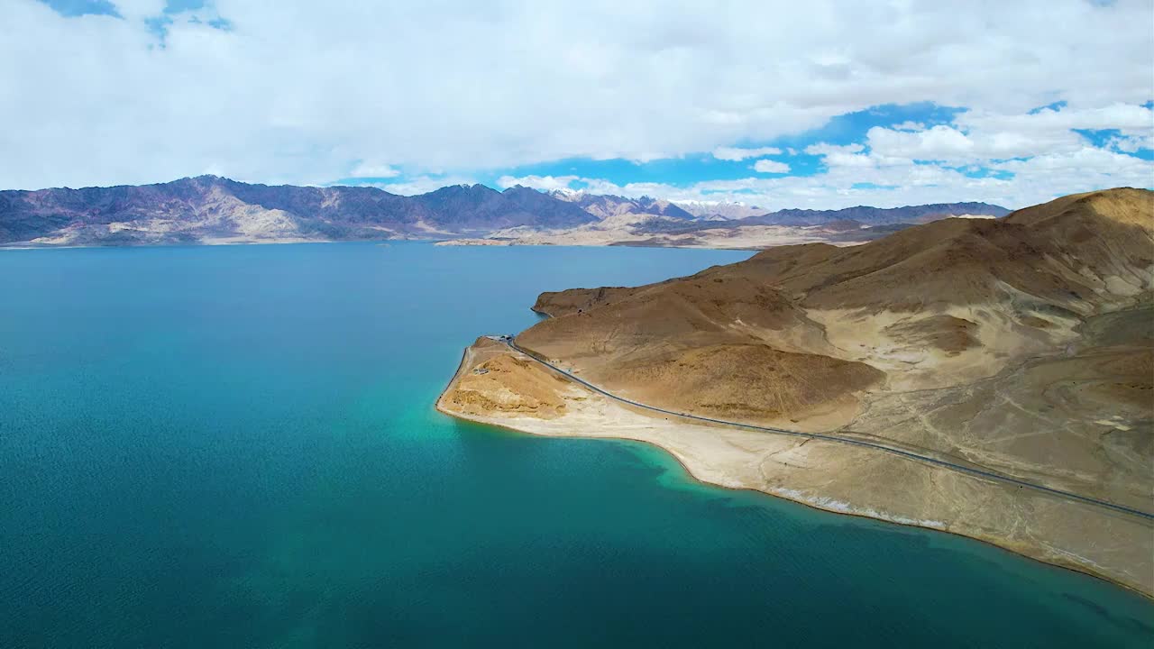 西藏阿里班公湖，六月晴朗的天气，航拍蓝天白云下，湖水湛蓝，雪山环抱，新藏公路从湖边经过。视频素材