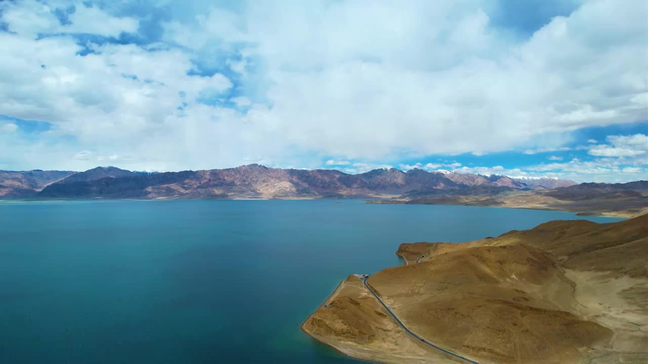 西藏阿里班公湖，六月晴朗的天气，航拍蓝天白云下，湖水湛蓝，雪山环抱，新藏公路从湖边经过。视频素材