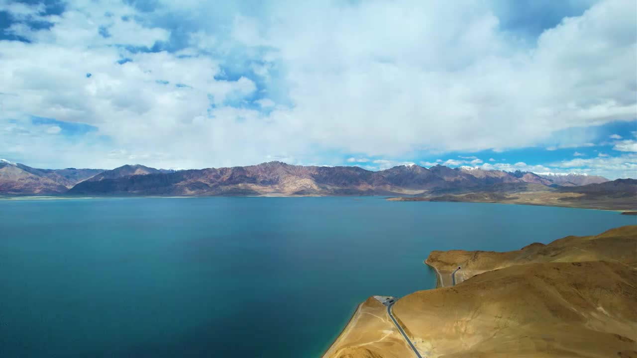 西藏阿里班公湖，六月晴朗的天气，航拍蓝天白云下，湖水湛蓝，雪山环抱，新藏公路从湖边经过。视频素材