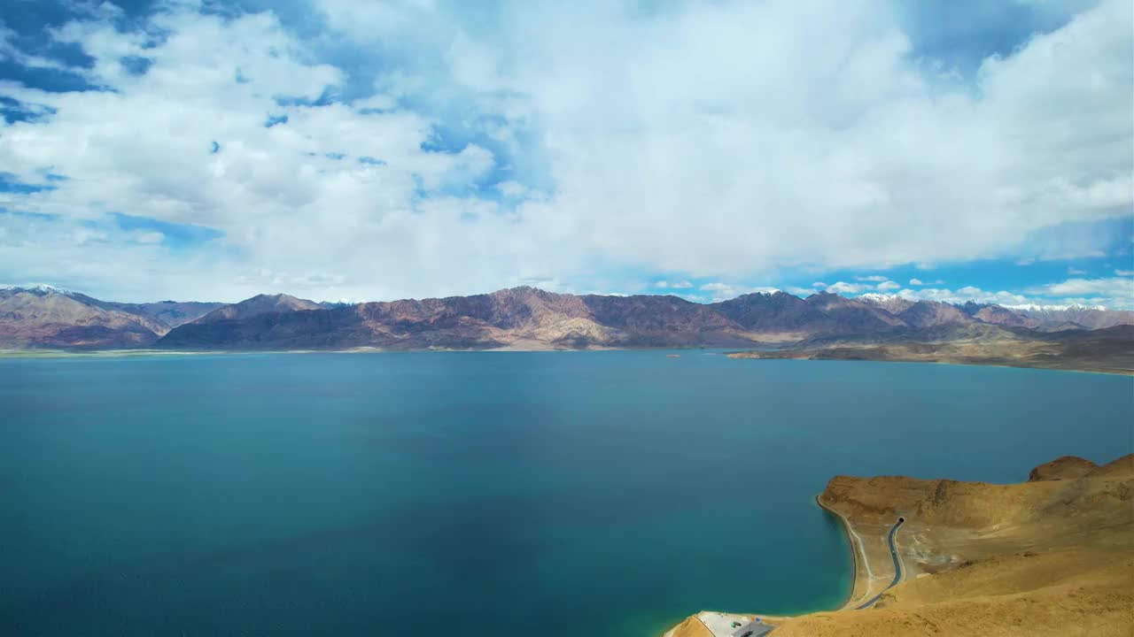 西藏阿里班公湖，六月晴朗的天气，航拍蓝天白云下，湖水湛蓝，雪山环抱，新藏公路从湖边经过。视频素材