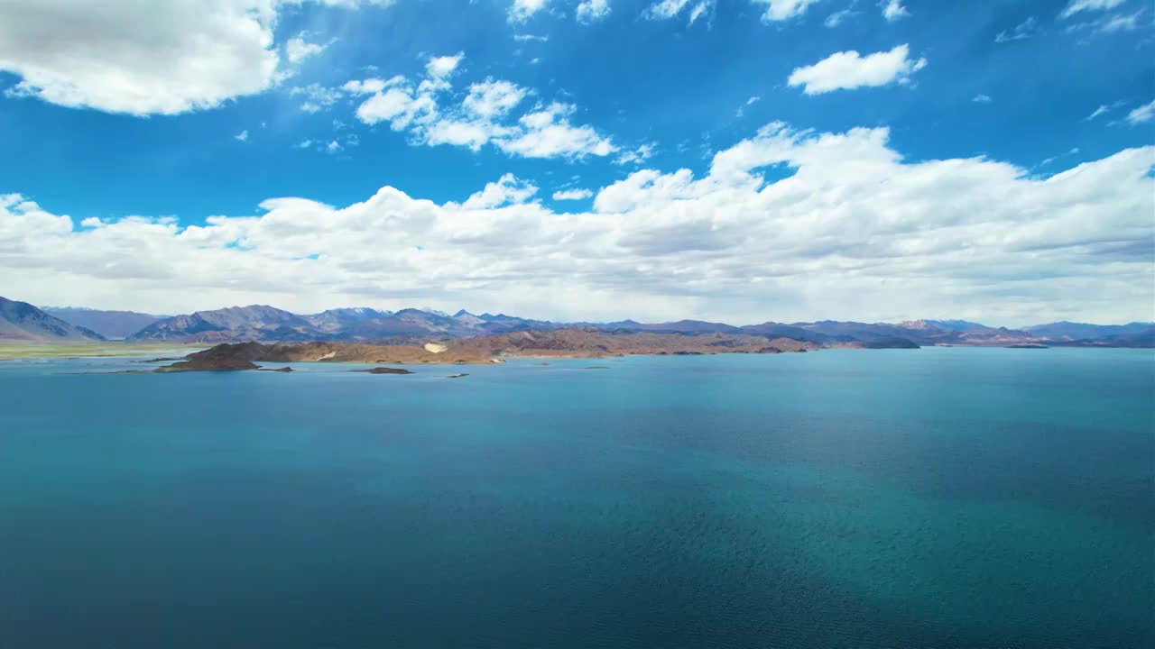 西藏阿里班公湖，六月晴朗的天气，航拍蓝天白云下，湖水湛蓝，雪山环抱，新藏公路从湖边经过。视频素材