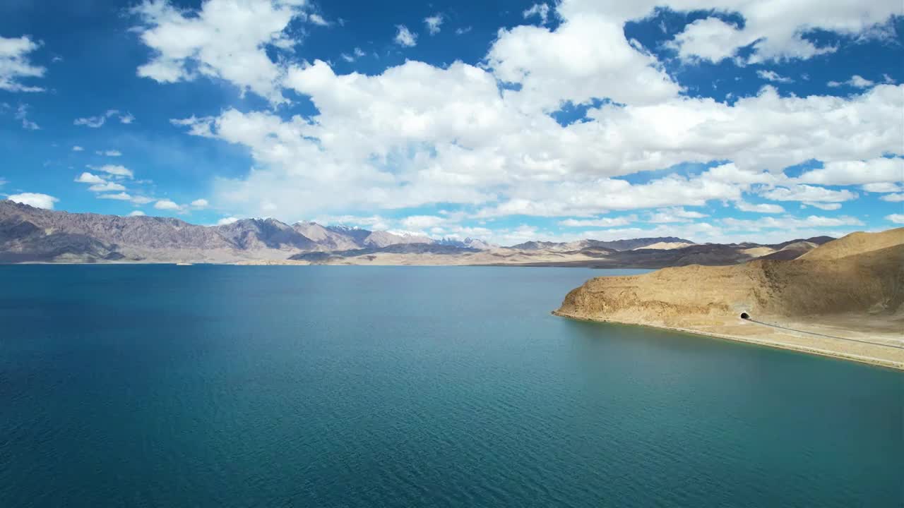 西藏阿里班公湖，六月晴朗的天气，航拍蓝天白云下，湖水湛蓝，雪山环抱，新藏公路从湖边经过。视频素材