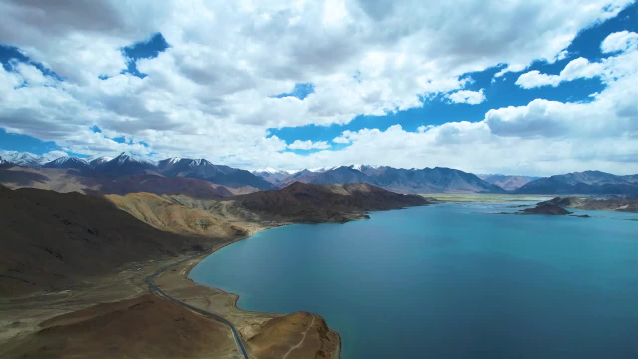 西藏阿里班公湖，六月晴朗的天气，航拍蓝天白云下，湖水湛蓝，雪山环抱，新藏公路从湖边经过。视频素材