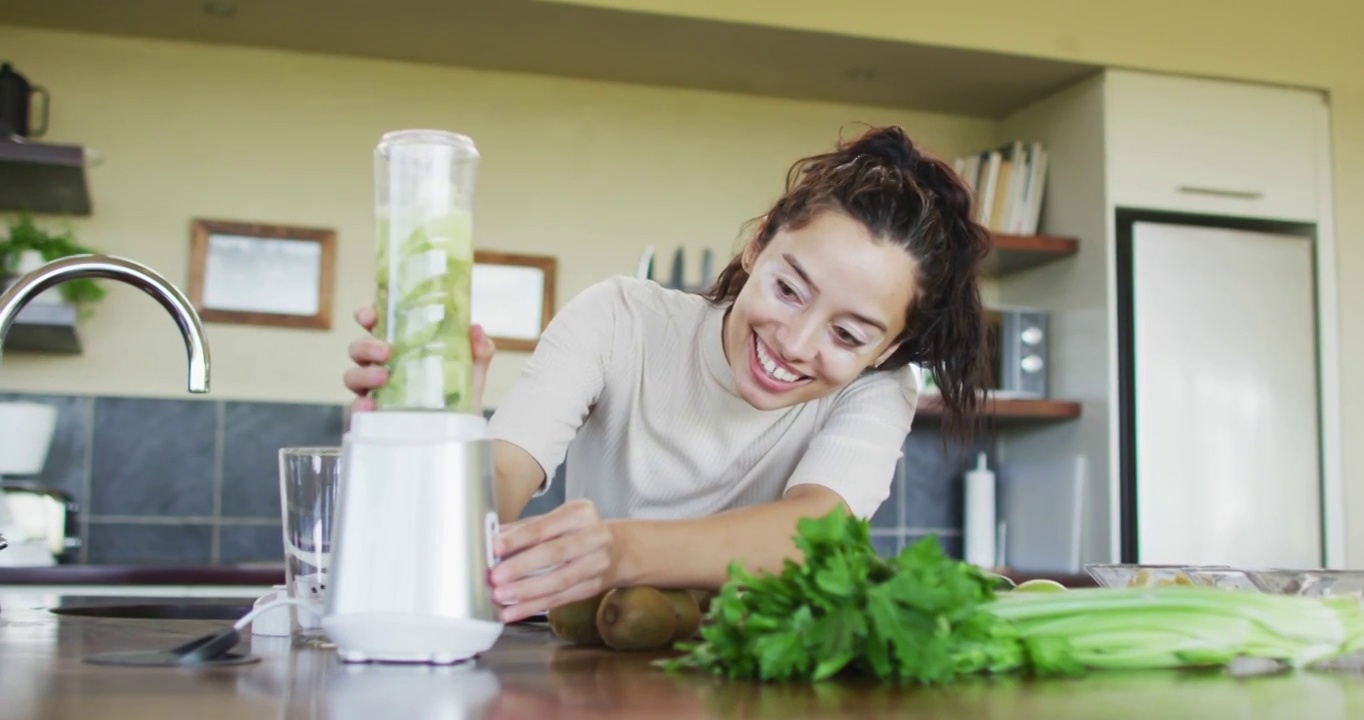 快乐的混血女人用搅拌机，在厨房准备冰沙视频素材