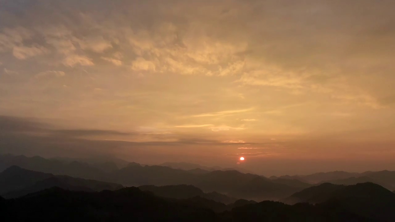 晨光中一轮红日从远山的天边喷薄而出，山谷中的云海蔓延山峦后，融入到了绯红的天际。视频素材