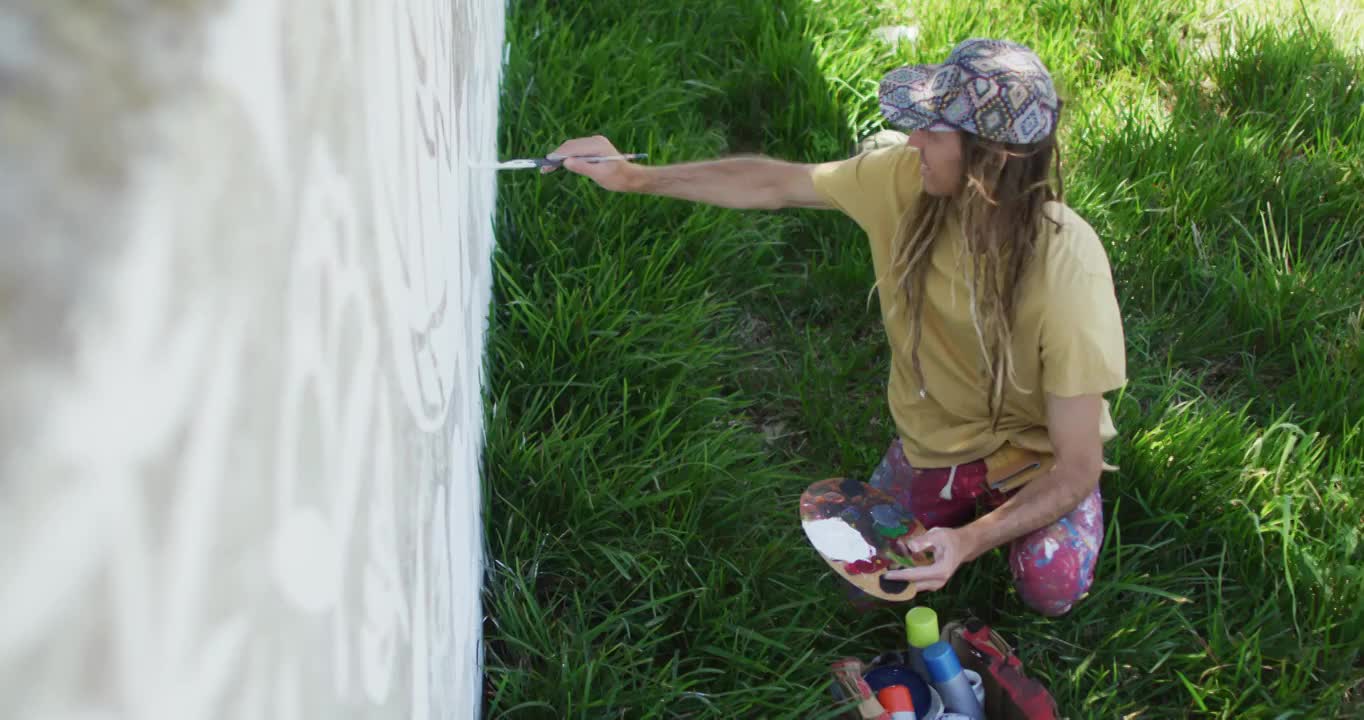 High angle video of caucasian male artist with dreadlocks painting mural on wall视频素材