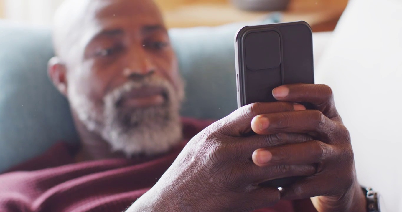 Happy senior african american man in log cabin, sitting on sofa and using smartphone, slow motion视频素材