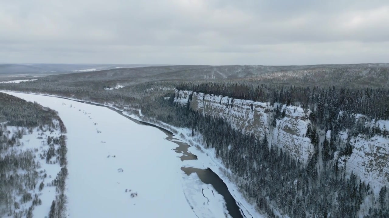冬季森林景观和生长在冰冻河流上悬崖上的松树林视频素材