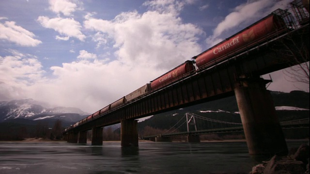 WS T/L货运列车在河上的桥上行驶，背景是山脉/沃特顿湖国家公园，阿尔伯塔，加拿大视频素材