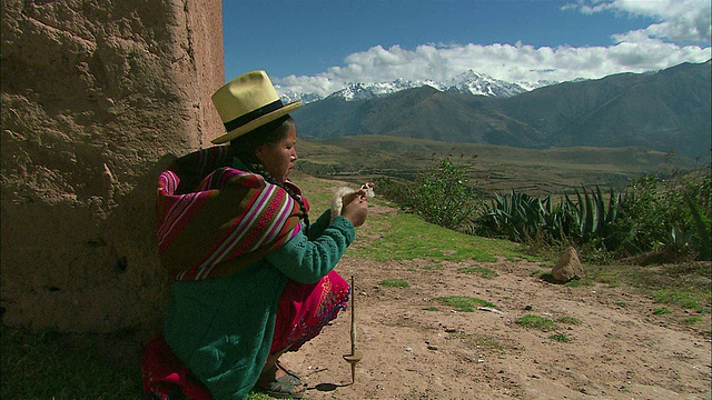 秘鲁库斯科地区山区的一名秘鲁妇女穿着色彩鲜艳的衣服，用纺锤来纺线视频素材