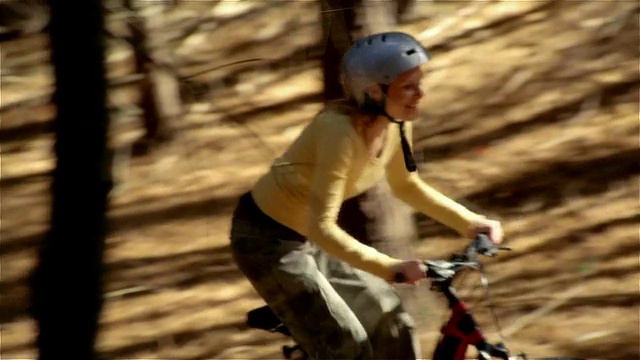 侧视图女人骑山地车上山在树林里视频素材