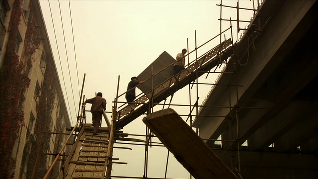 低角度广角拍摄的建筑工人在建筑工地的斜坡上行走/中国北京视频素材