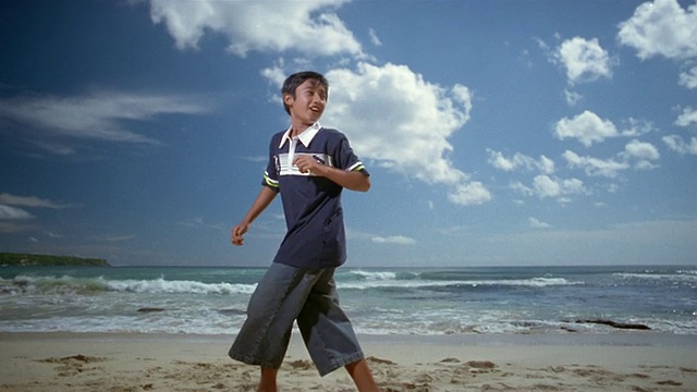 慢动作中镜头男孩踢在海滩上的球，海浪翻滚在/印尼巴厘岛视频素材