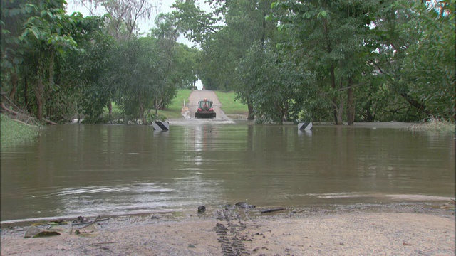 洪水淹没了一条道路，一辆拖拉机正在清除河水/澳大利亚北部阿德莱德河视频素材