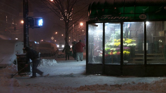 一个男人晚上在一家花店外的街角铲雪。视频素材