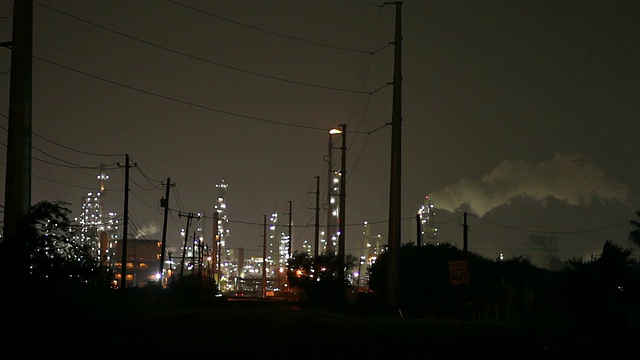 炼油厂的烟囱里冒出滚滚浓烟，在夜晚灯火通明，汽车在前景中穿行视频素材