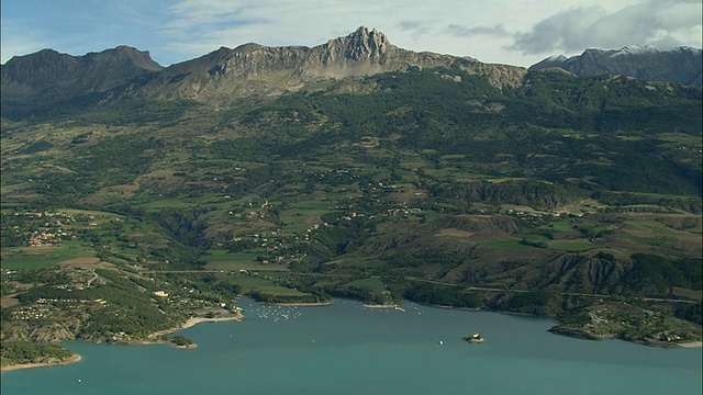 空中村庄靠近Lac de Serre-Poncon海岸，水上有船，公路上有交通，法国阿尔卑斯-滨海视频素材