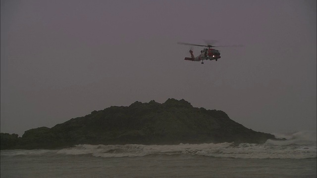 长镜头静态-一架海岸警卫队直升机盘旋在一个被风暴海浪冲击的岩层上视频素材