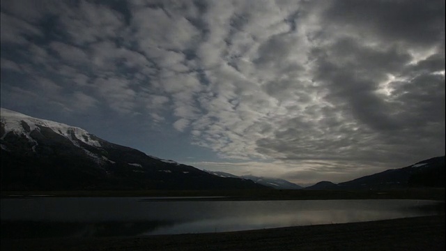 广角，锁定-云漂移在海湾和雪山上，当白天变成夜晚/加拿大视频素材