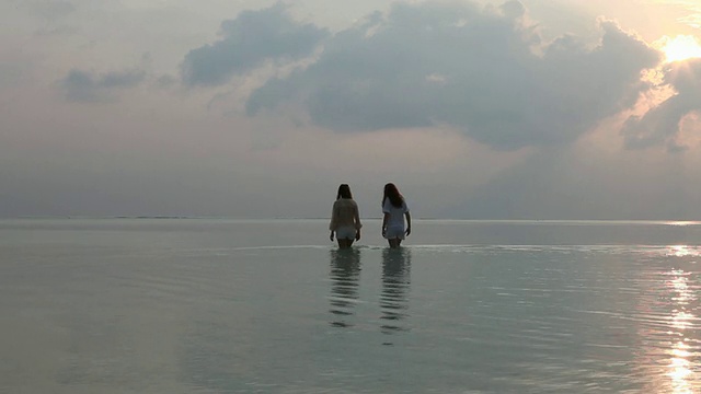 十几岁的女孩在日落时走过浅浅的泻湖水视频素材